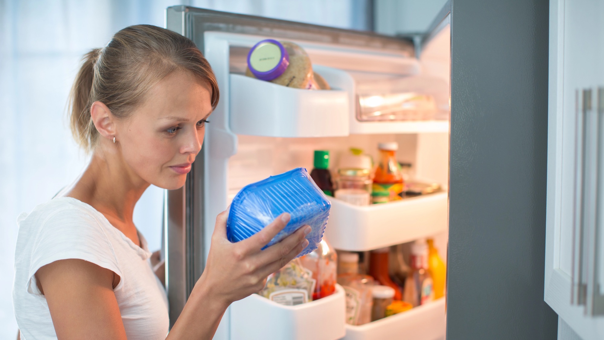 woman inspects food while fridge is open in front of her