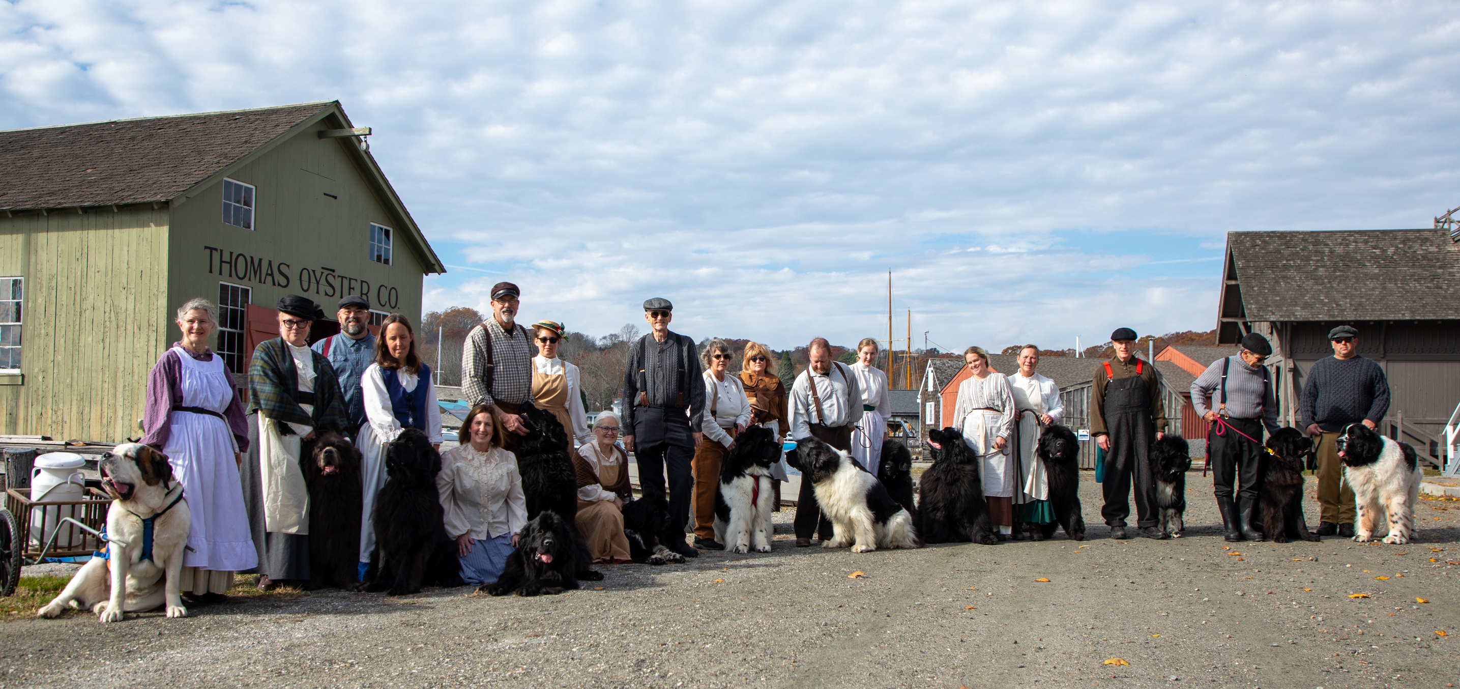 several people dressed in 19th century clothing stand with large dogs