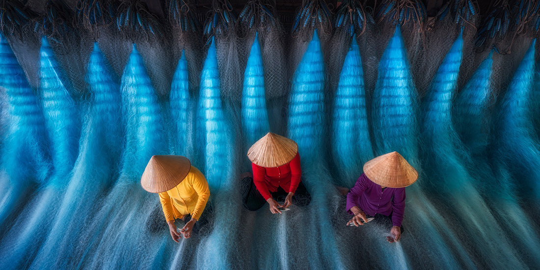 three women wearing bamboo sun hats fix fishing nets