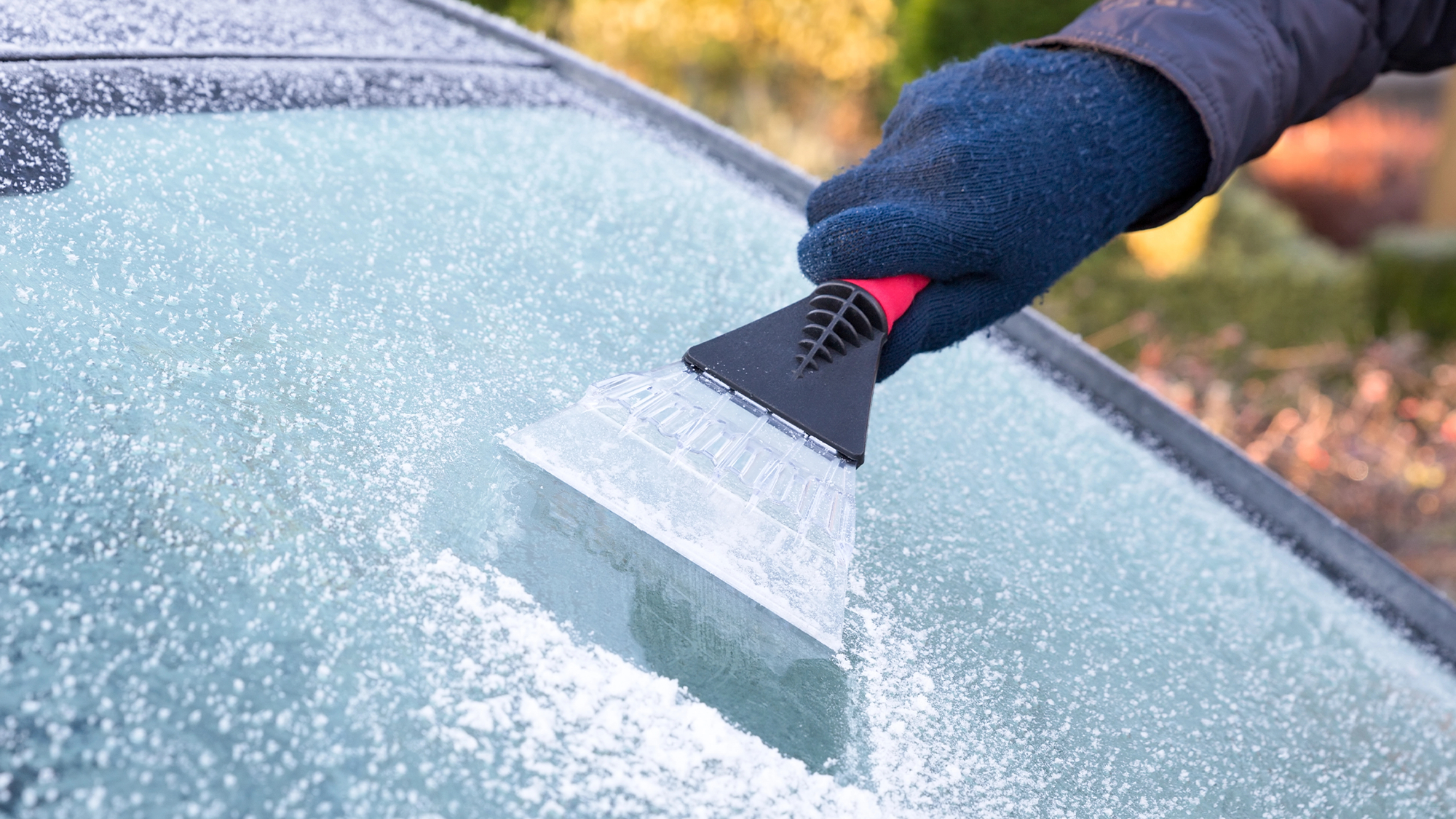 a gloved hand scraping a frosty windshield