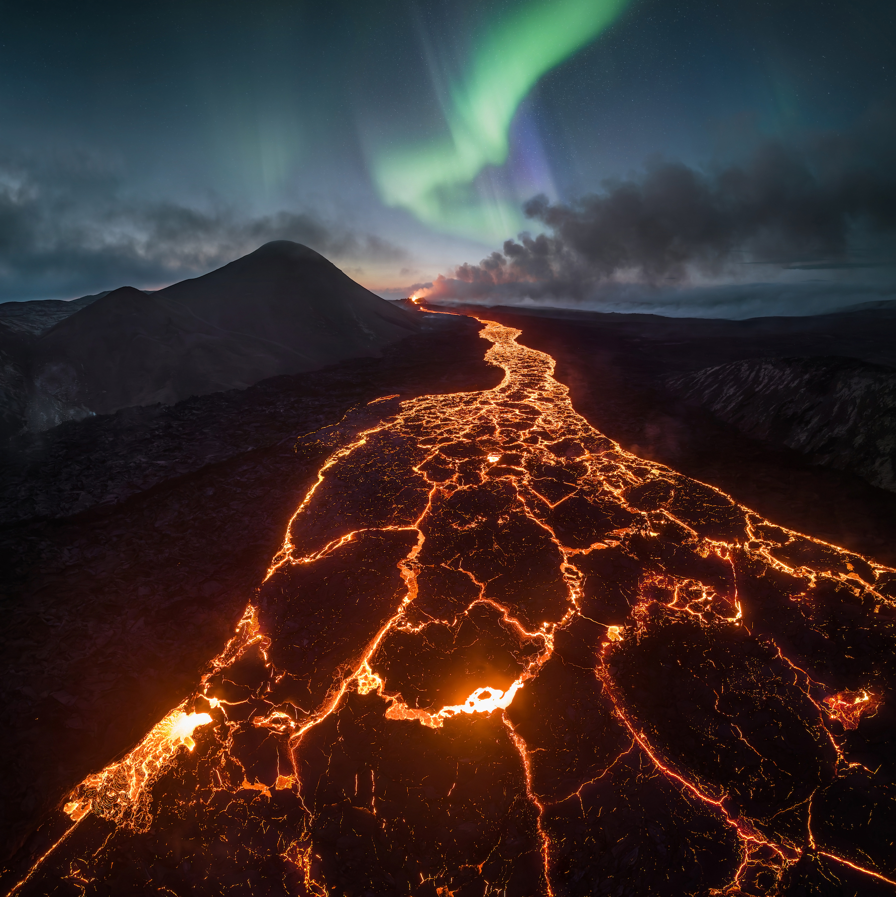 a river of lava moves under an aurora in Reykjanesbaer, Iceland