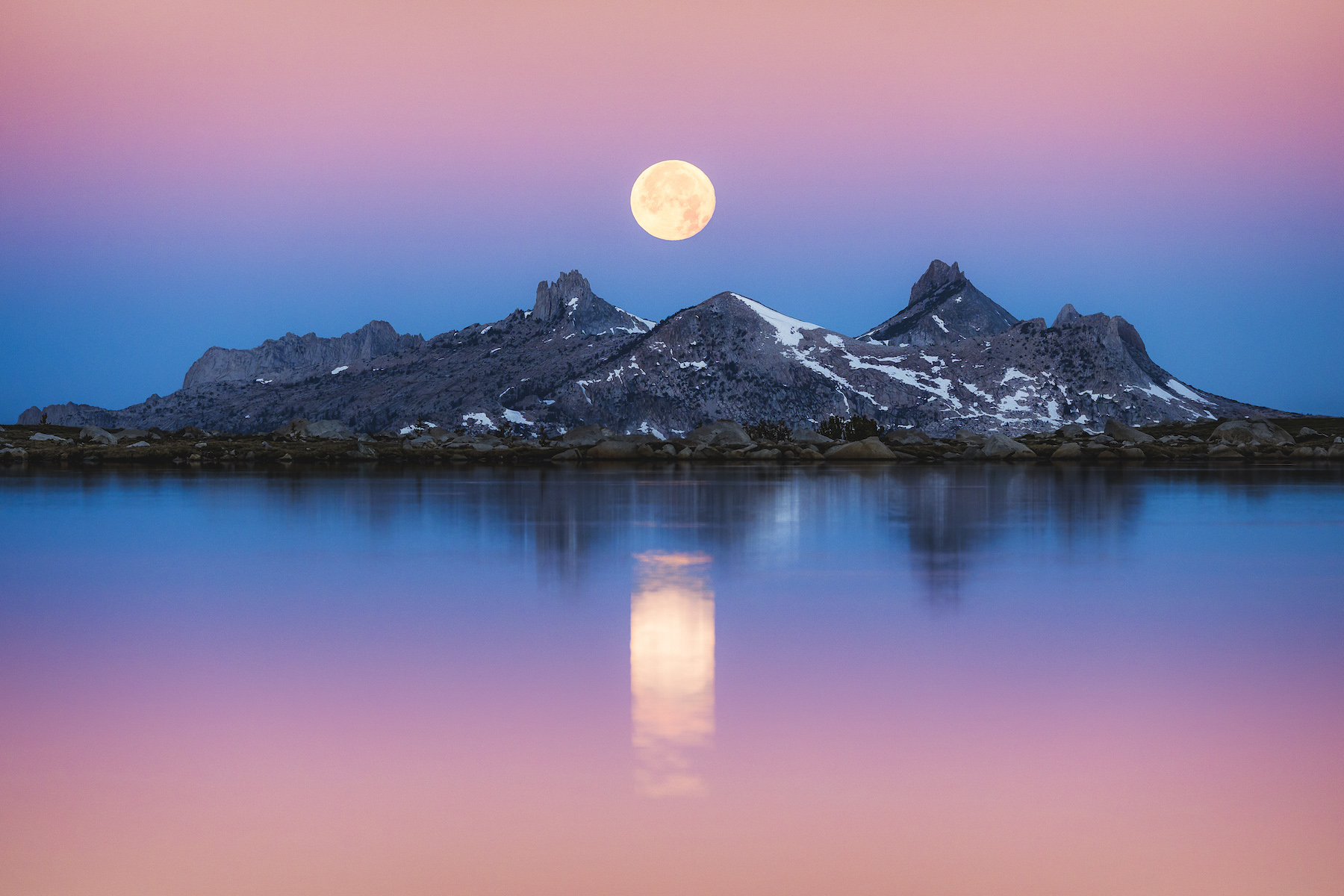 a moon rises over mountains in front of a lake in Yosemite National Park, California