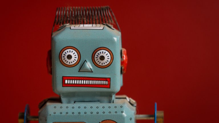 The book "Raising AI" by De Kai serves as an essential guide for parenting our future, exploring the profound responsibilities of nurturing artificial intelligence. The cover features a minimalist, metallic silver aesthetic that mirrors the clinical yet evolving nature of technology. In contrast to this futuristic outlook, the image of a weathered vintage tin robot—with its wide-eyed, staring expression and rusted edges—highlights the human-centric "mirage" of ethical AI, reminding us of the mechanical origins and imperfect projections we cast upon our digital creations.