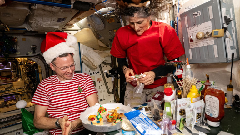 two astronauts in santa hats and reindeer antlers sit around a table with christmas cookies
