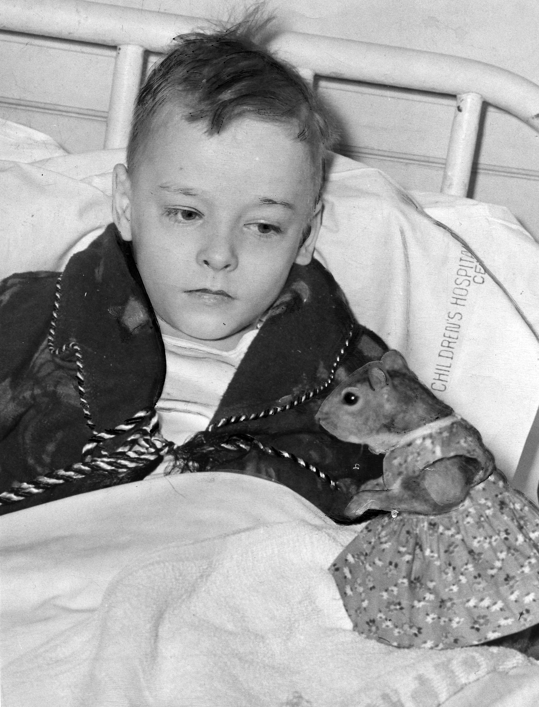 A black-and-white historical photograph of a young boy in a hospital bed at the Children's Hospital Center in Washington, D.C. The boy, wearing a dark patterned robe, looks down at Tommy Tucker, a pet squirrel dressed in a floral-print dress. The squirrel is positioned on the bed covers, and the hospital's name is partially visible on the white pillowcase behind the boy.