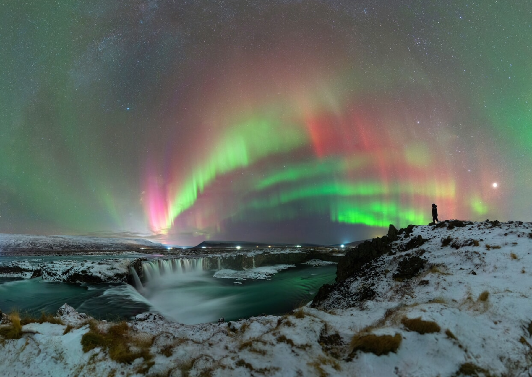 a green and red aurora over a waterfall