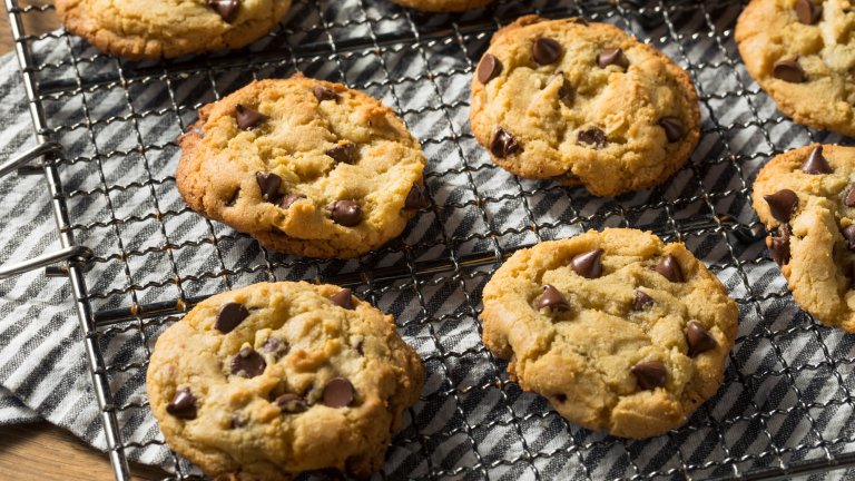 Four chocolate cookies are shown cooling on a wire rack after coming out of the oven.