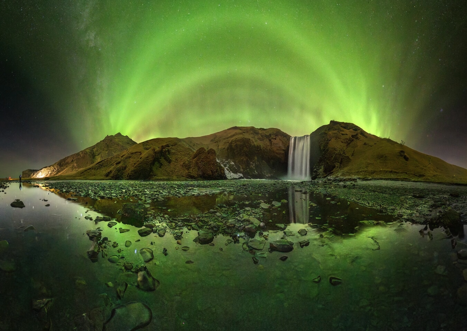 a bright green aurora over a waterfall and reflecting in a stony pool