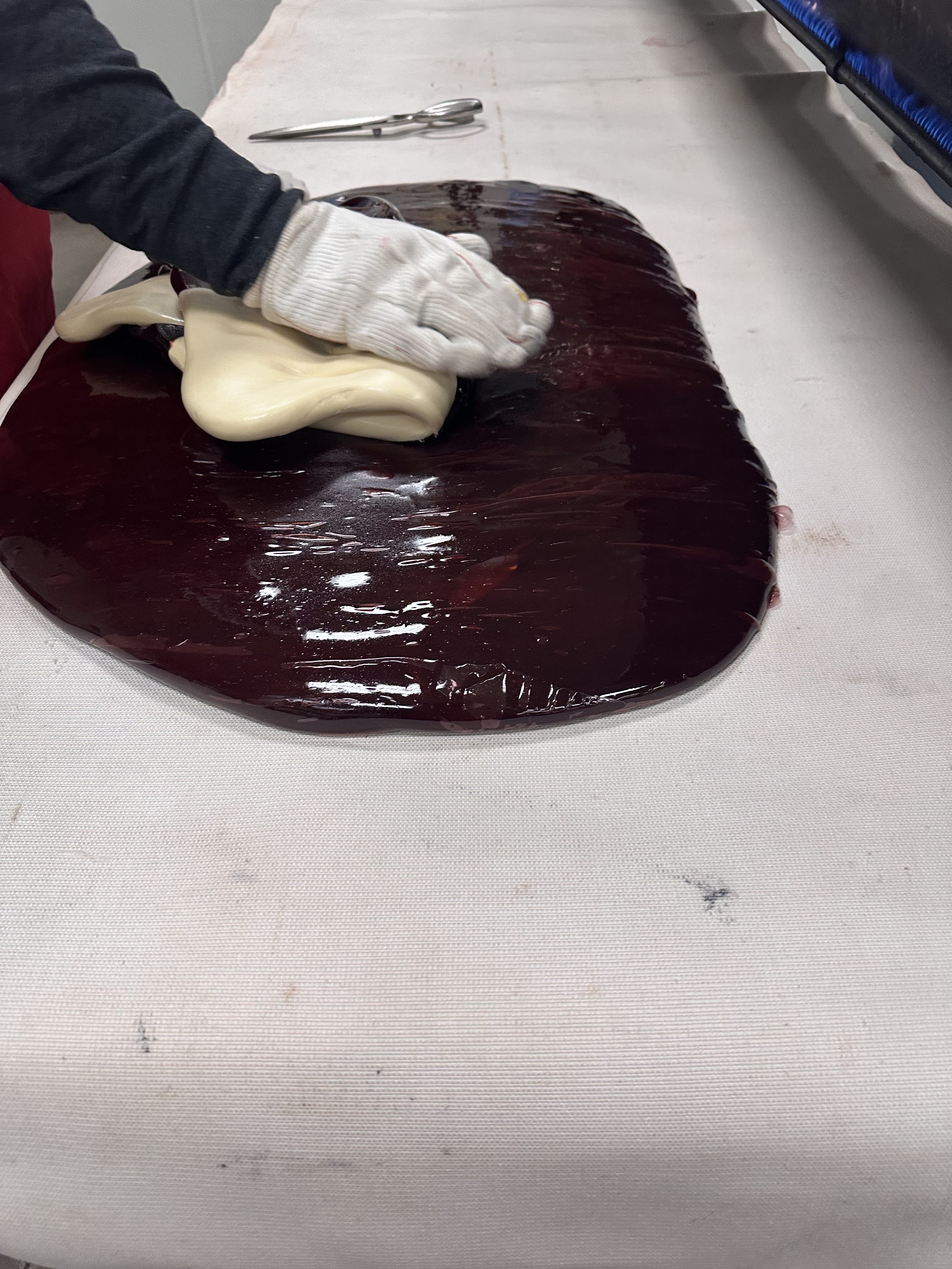 a candy maker rolls in a white center of a candy cane into some red liquid