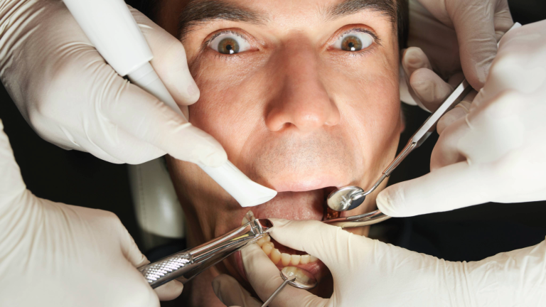 a scared man with several dental tools in his mouth