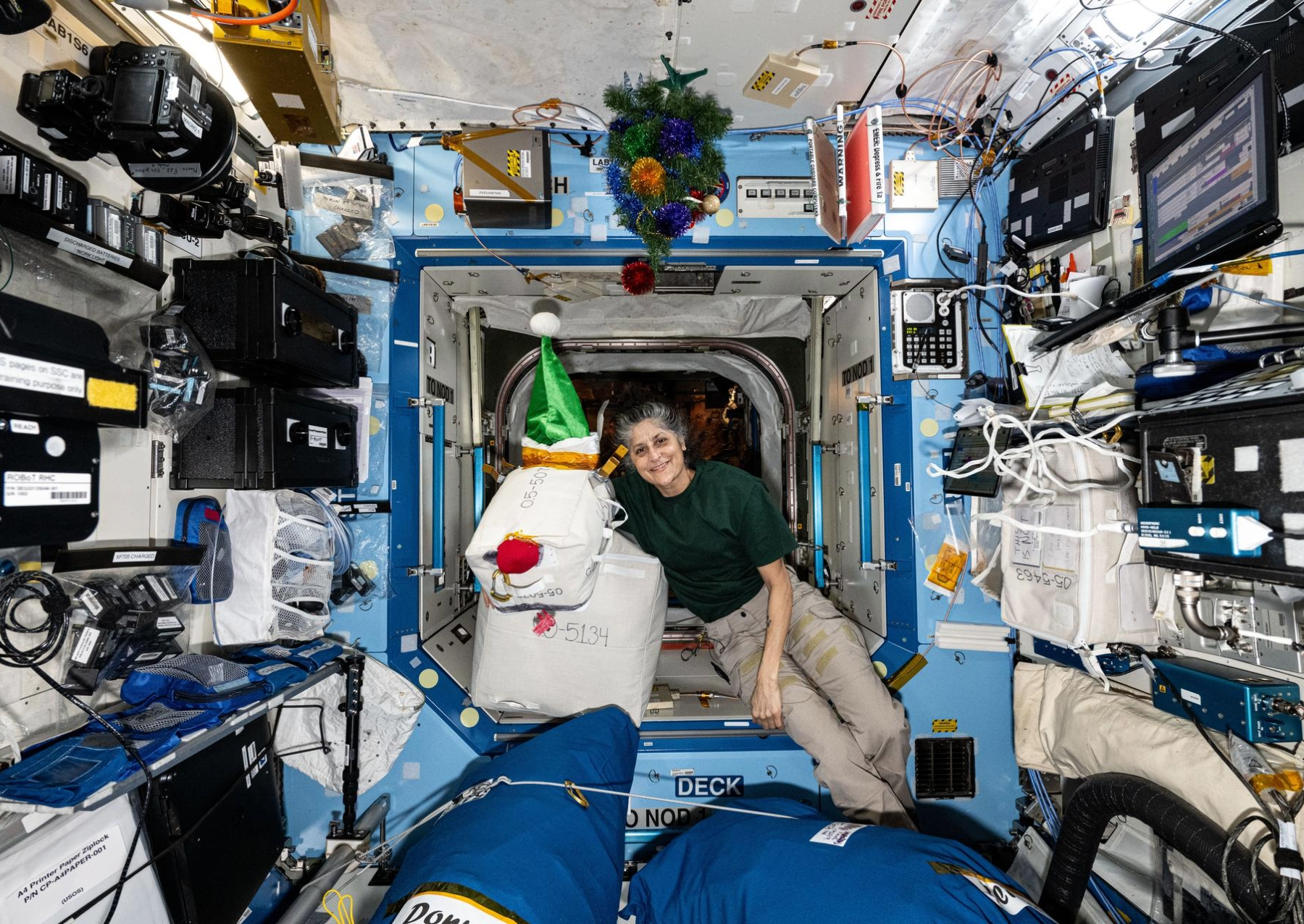 a female astronauts holds a christmas decoration made with white plastic bags and red nose to look like rudolph the red nosed reindeer