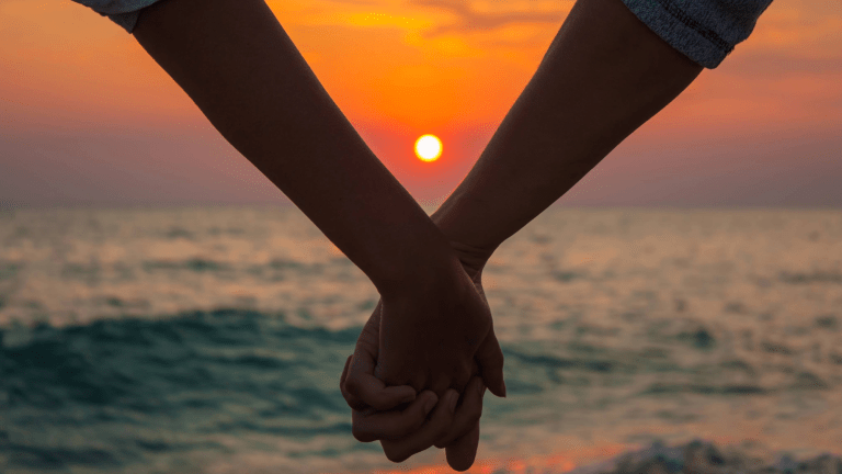a couple holding hands as the sun sets over water