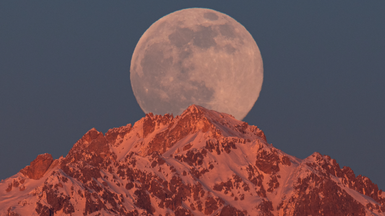 a full moon rises over a snowy mountain
