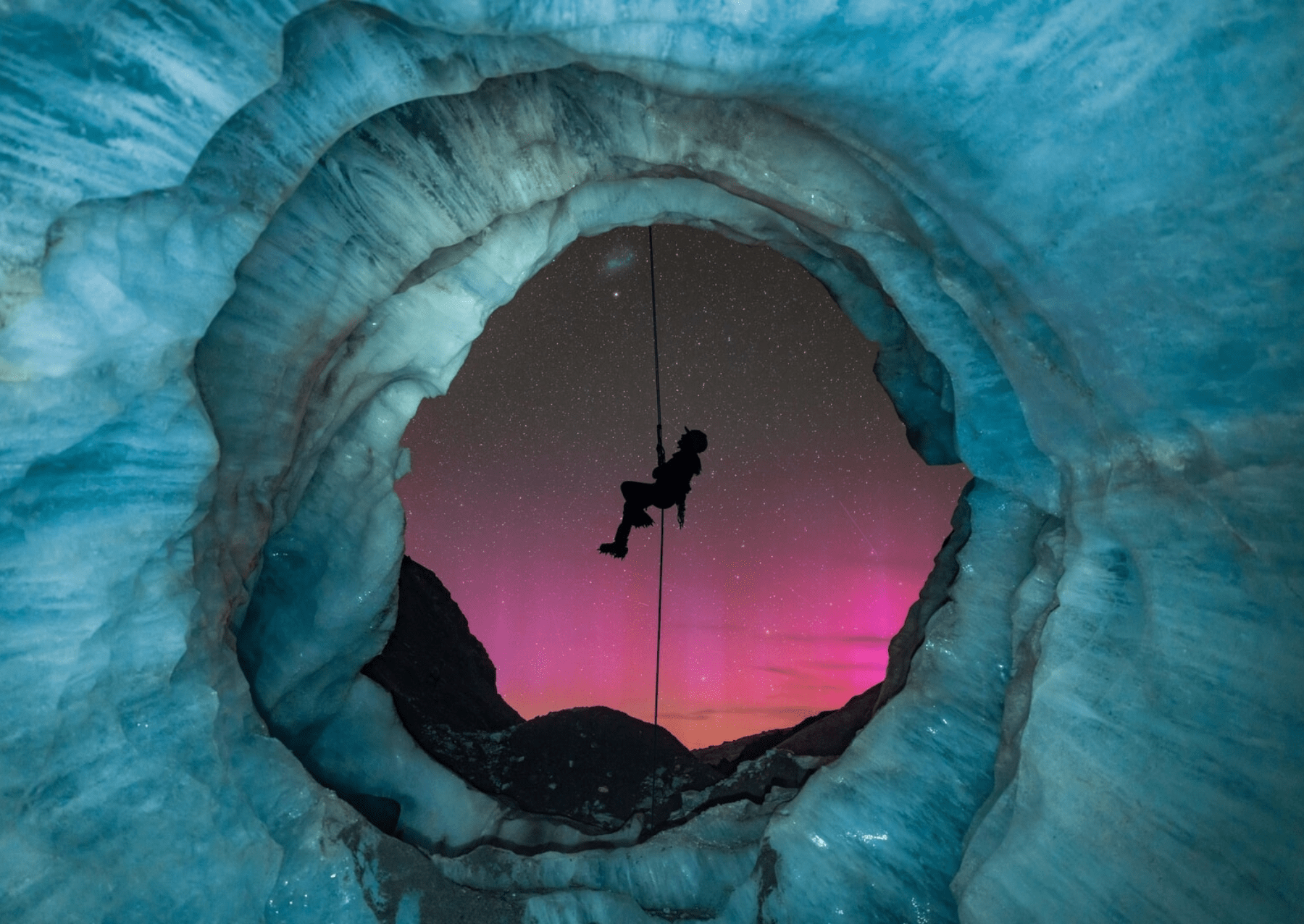 a pink aurora shining through light blue ice