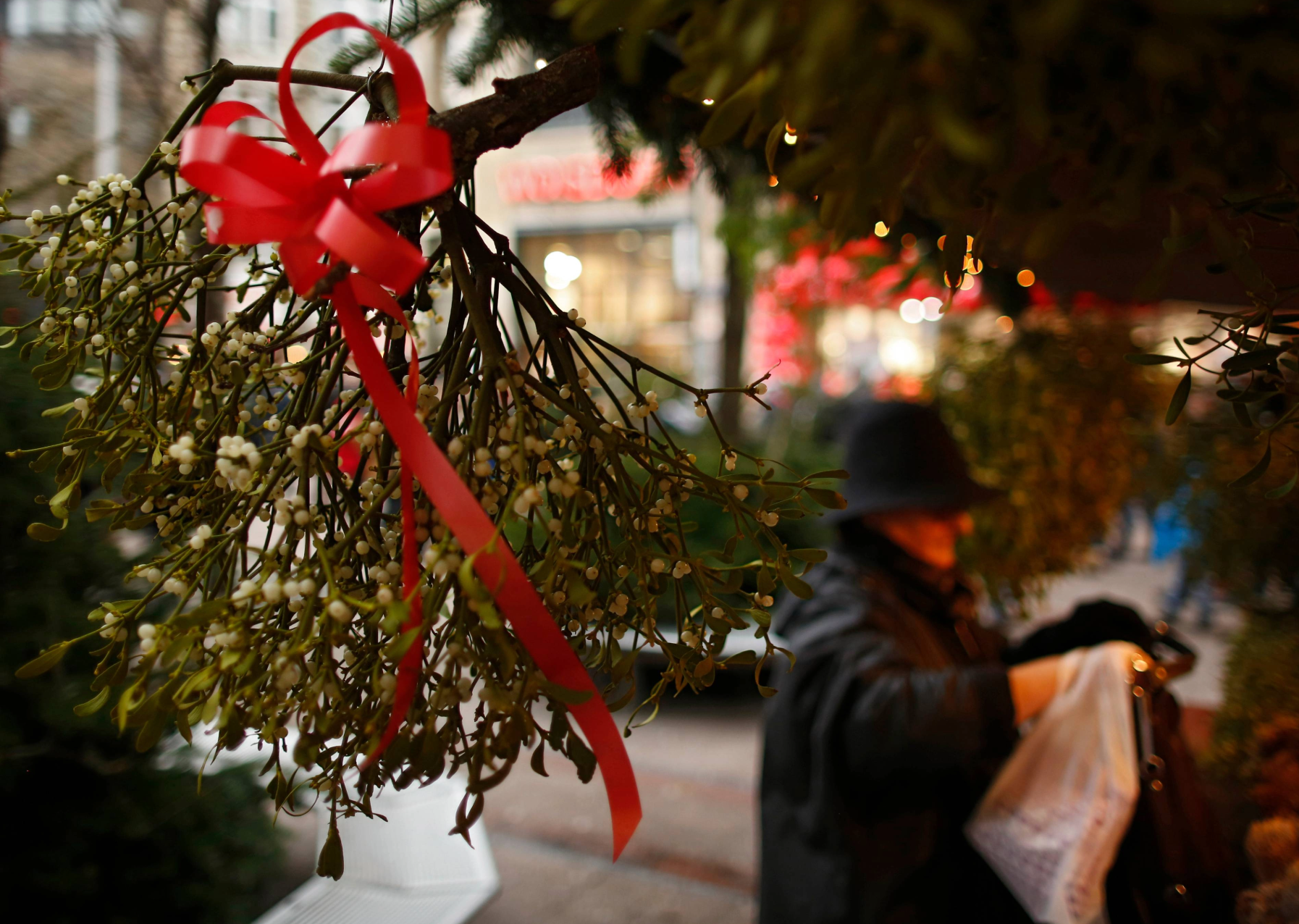 a woman in a christmas market looking at mistletoe. it is a green shurub with white berries and tied with a red ribbon