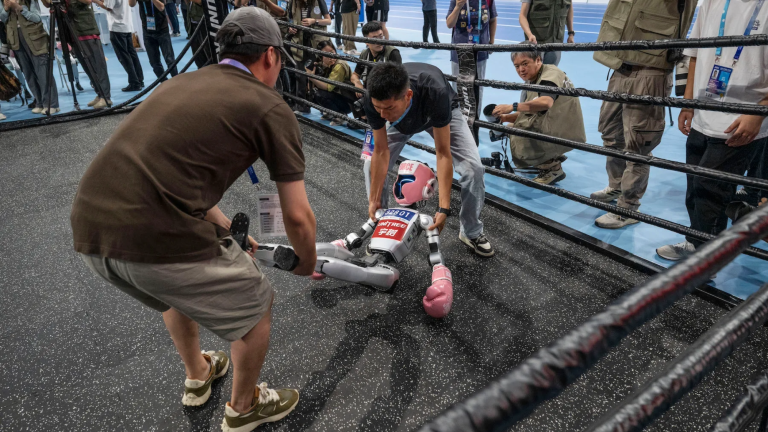 A humanoid robot is carried by technicians after being knocked out in a kickboxing match at the World Humanoid Robot Games on August 15, 2025 in Beijing, China.