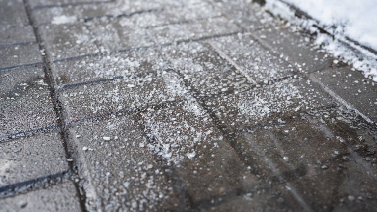 Anti-icing chemicals in winter season. Street treated with technical salt or de-icing chemicals, closeup view. Effective tool to fight ice on surfaces. Rock salt on road.
