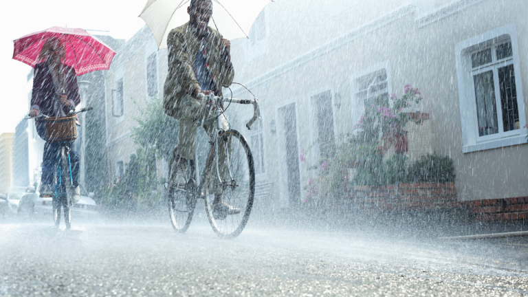 a couple riding bikes in the pouring rain while holding umbrellas