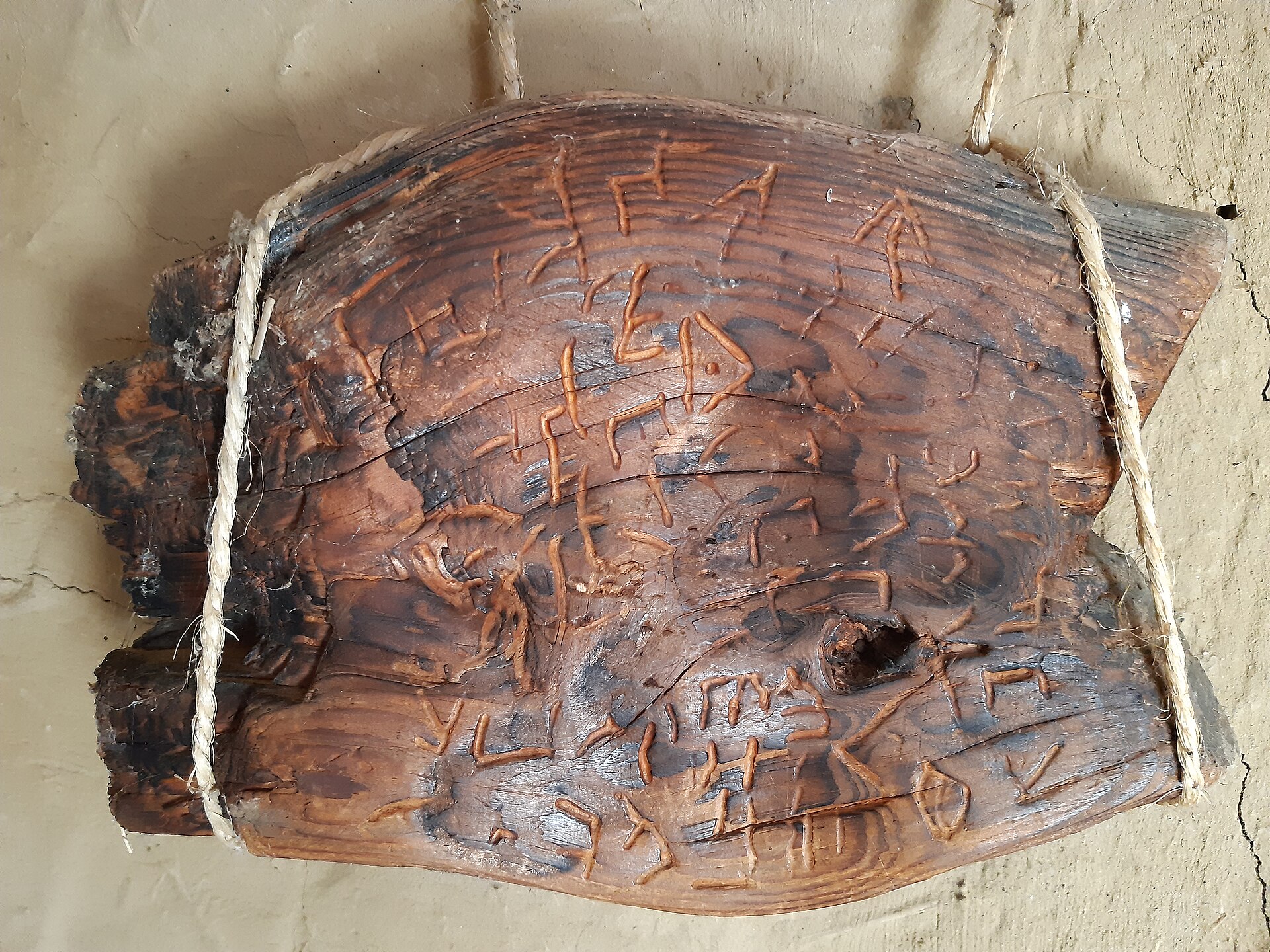 A piece of wood etched with symbols suspended on a wall with twine.