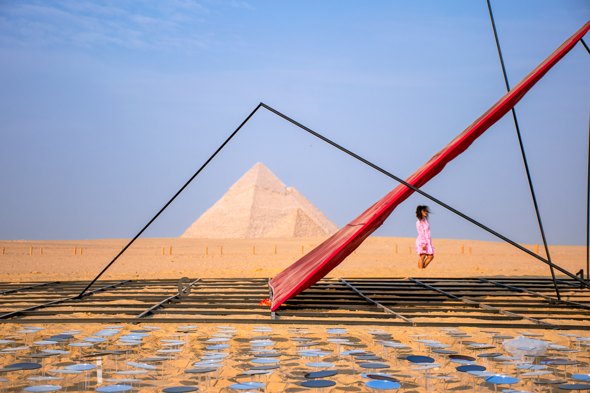 A modern triangular sculpture frames the Great Pyramid, accented by bold red fabric and a field of mirrors. The photographer sought to capture the harmony between the stark lines of the installation and the ‘eternal shape of the pharaoh’s tomb’, creating a ‘geometric interplay of past and present’.
