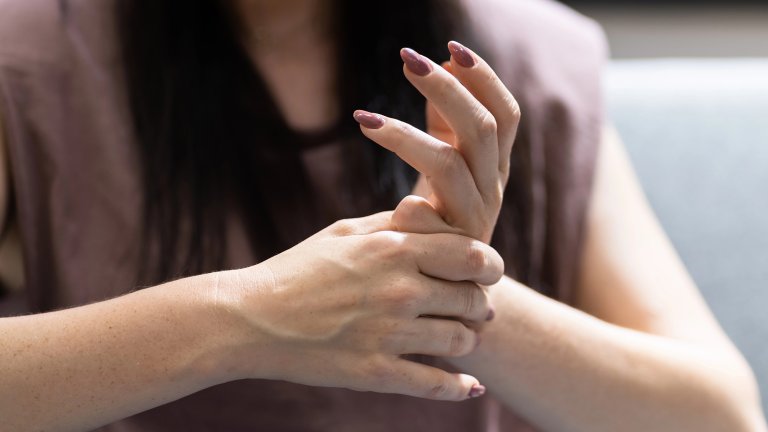 A white woman cracks her fingers. She has muted purple nail polish on and a muted purple blouse on, too.