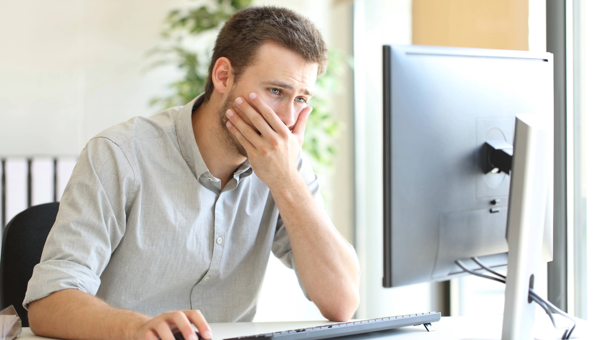 a man anxiously sitting in front of a computer with his hand over his mouth