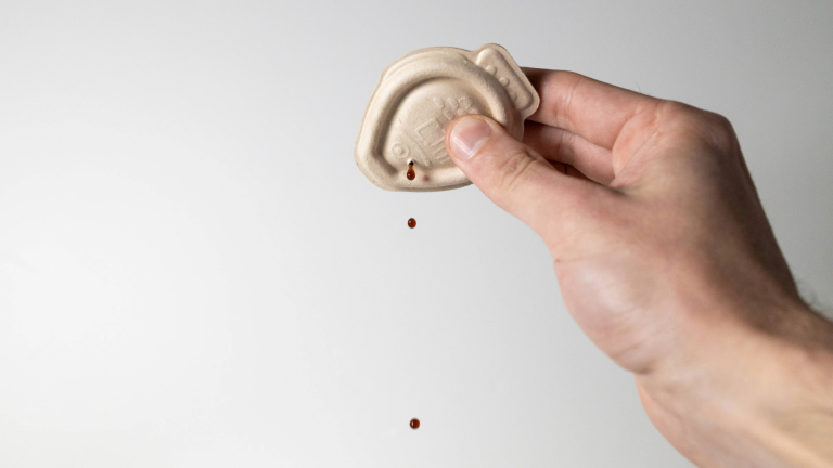 a hand squeezes a fish-shaped soy sauce container as brown droplets come out of it