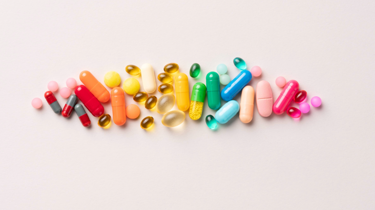 pills of various sizes laid out in red, orange, yellow, green, blue, and pink order