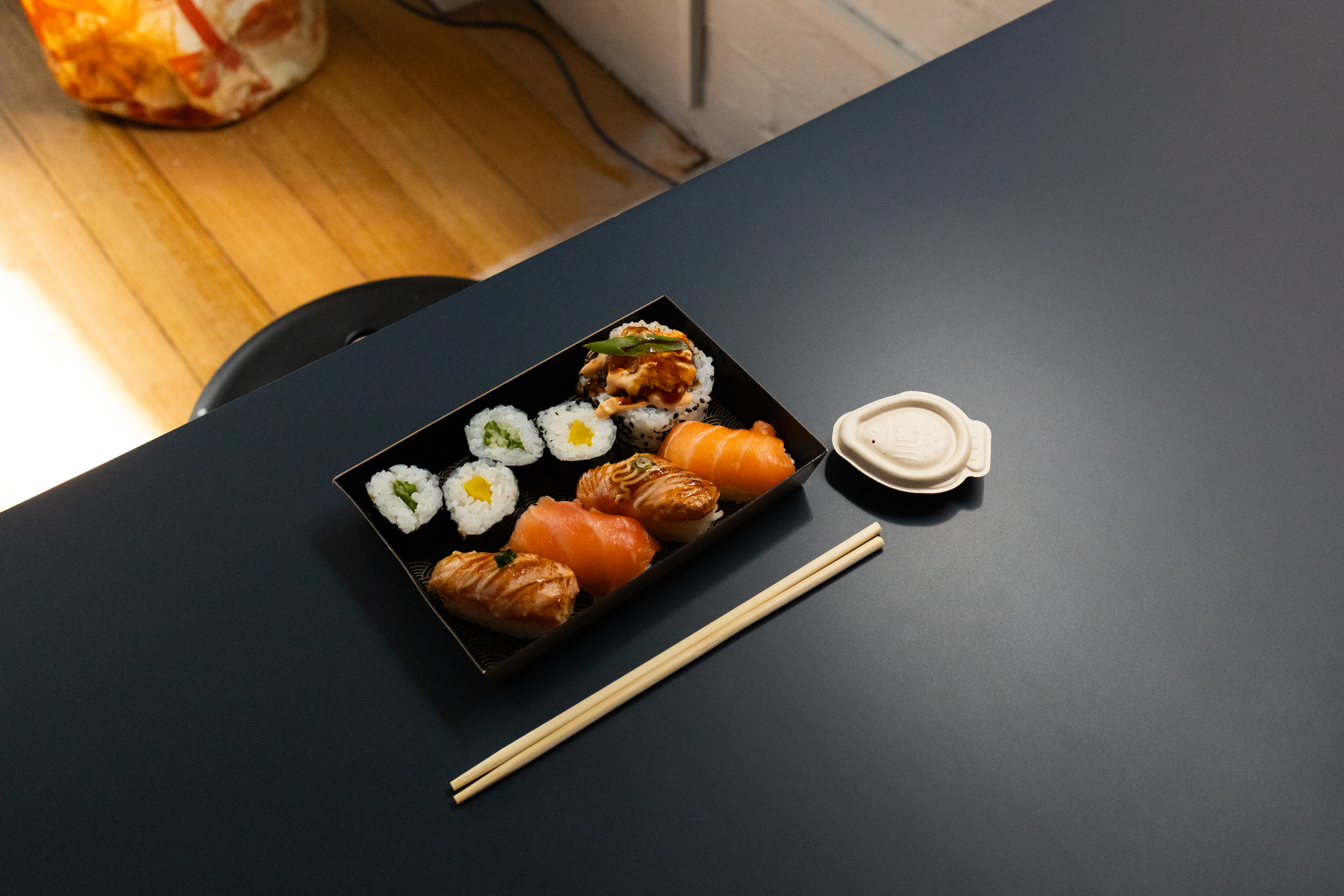 a plate of sushi on a black tables, with chopsticks and a fish-shaped soy sauce continer