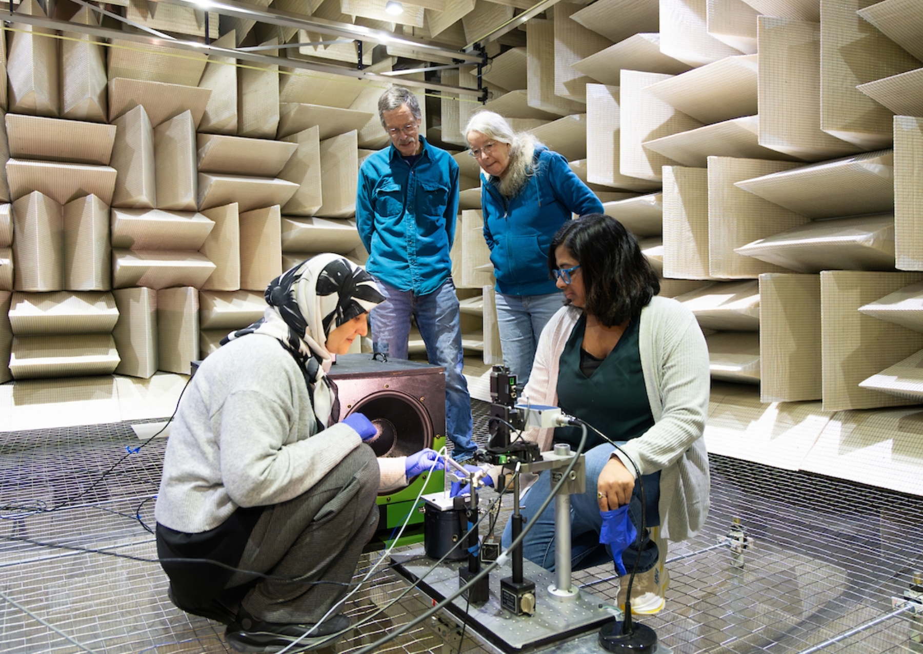 two students stand over a machine testing it while two advisors look on