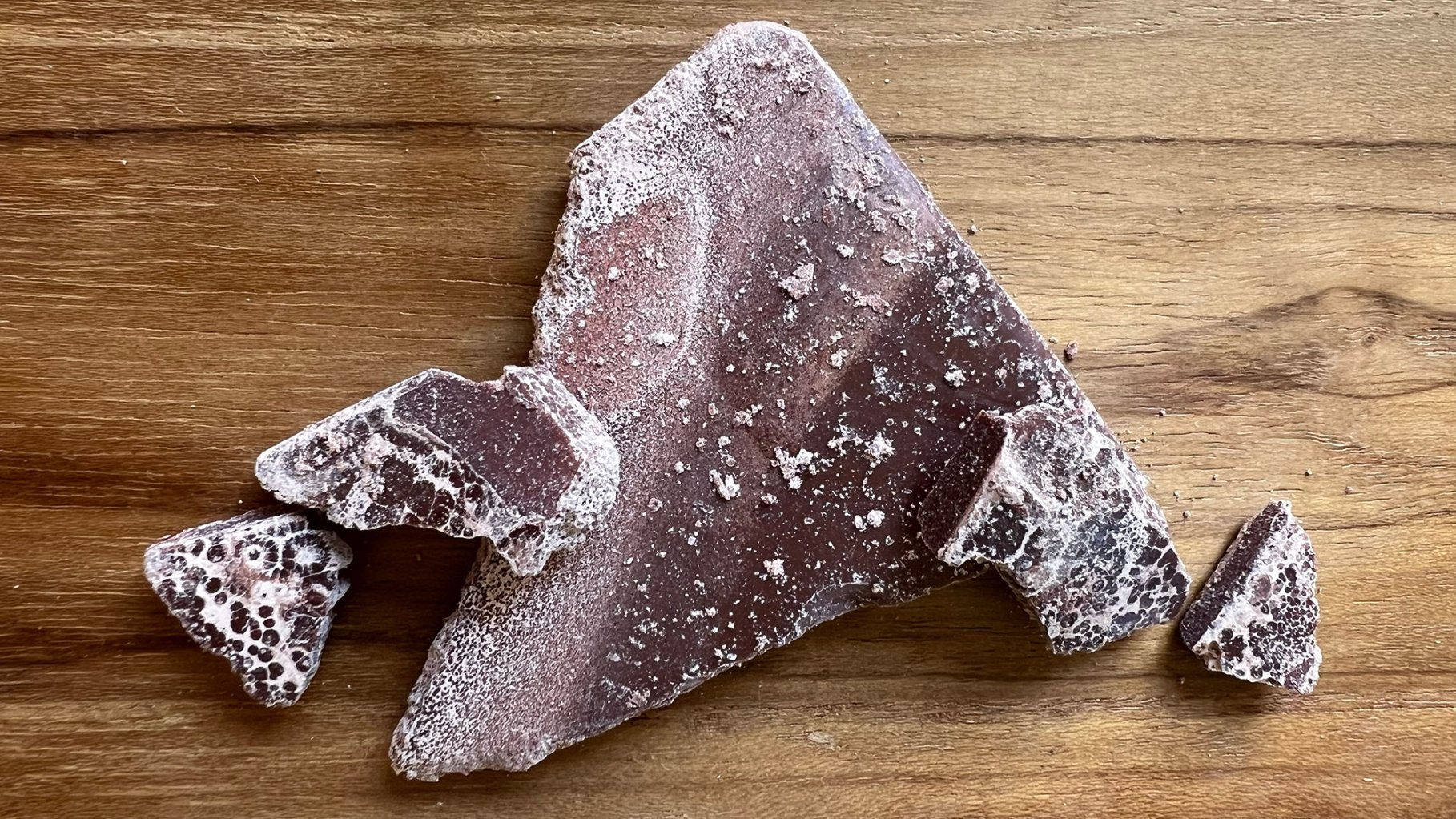 Some pieces of chocolate with white splotches on a wooden cutting board.