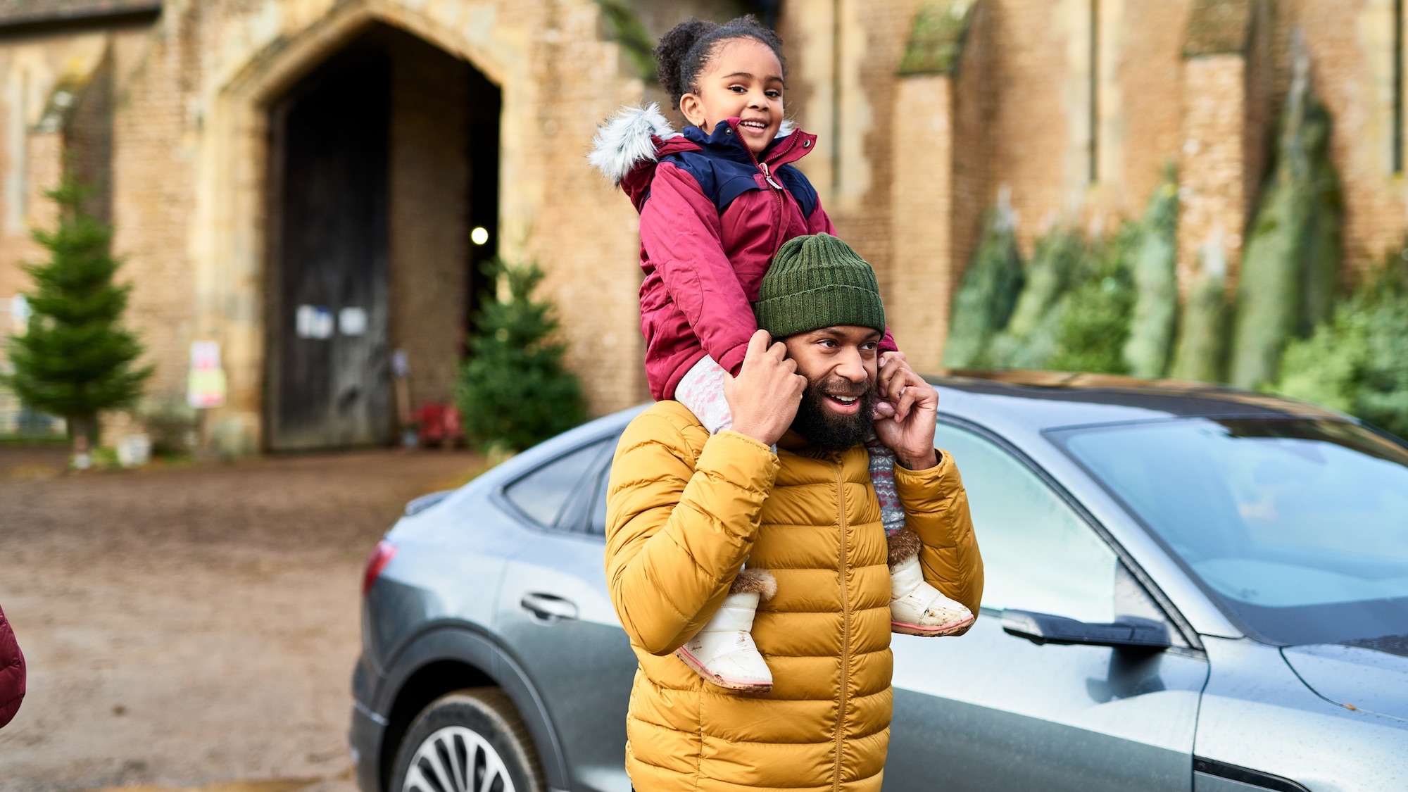 Young girl on dad's shoulders next to car at a Christmas tree farm, childhood, excitement, holiday season
