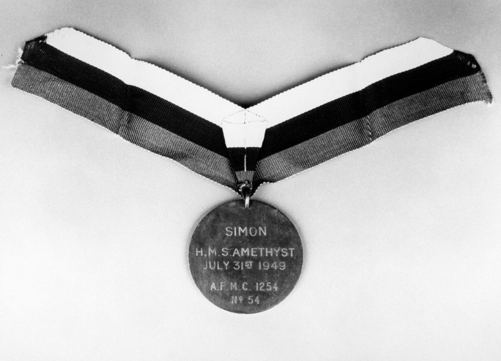 A black-and-white close-up of the Dickin Medal awarded to Simon. The circular bronze medal is suspended from a striped ribbon. The inscription on the medal reads:

SIMON

H.M.S. AMETHYST

JULY 31ST 1949

A.F.M.C. 1254

Nº 54