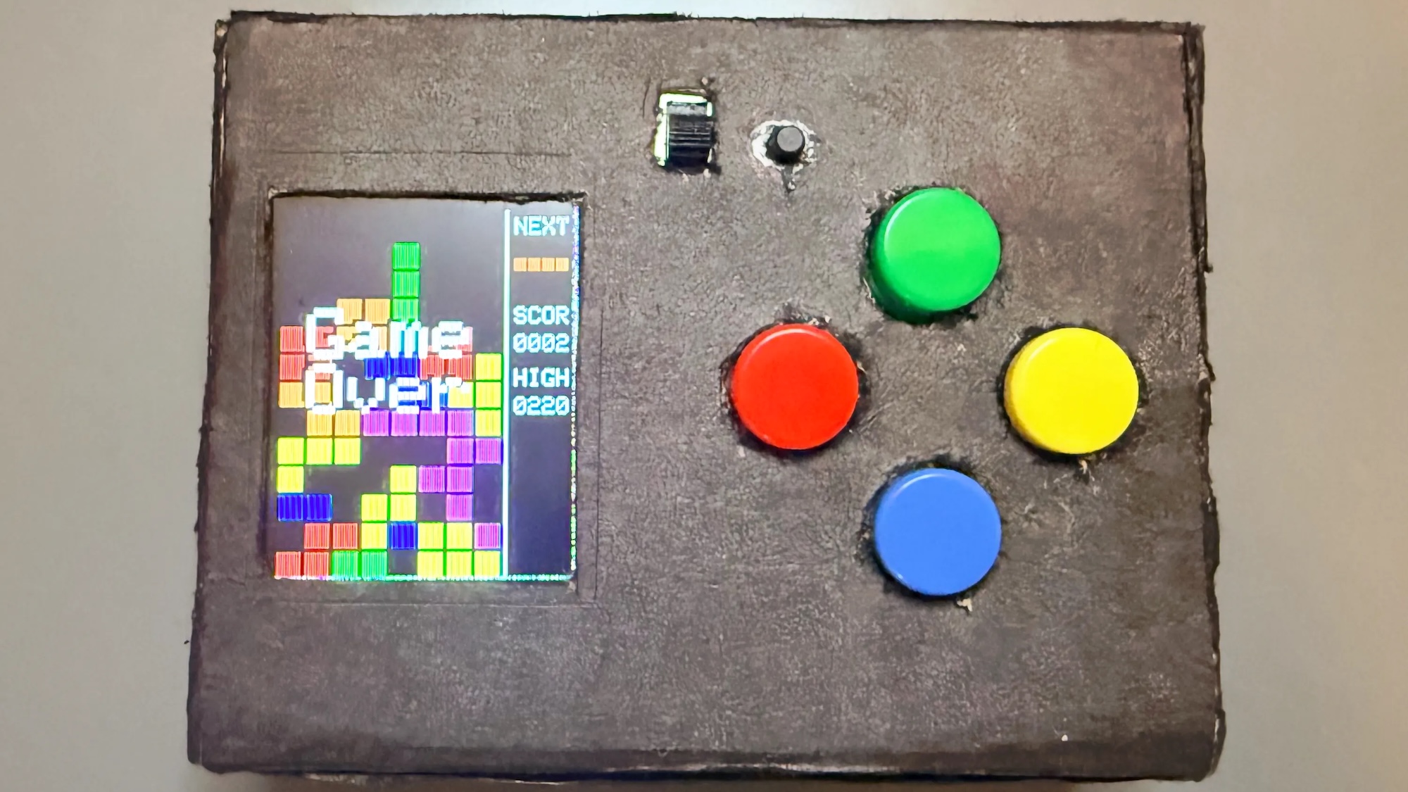 A homemade cardboard box containing a Tetris game and four buttons