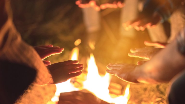 Hands warming near a bonfire at night