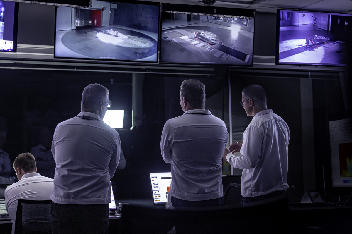 three men watch monitors