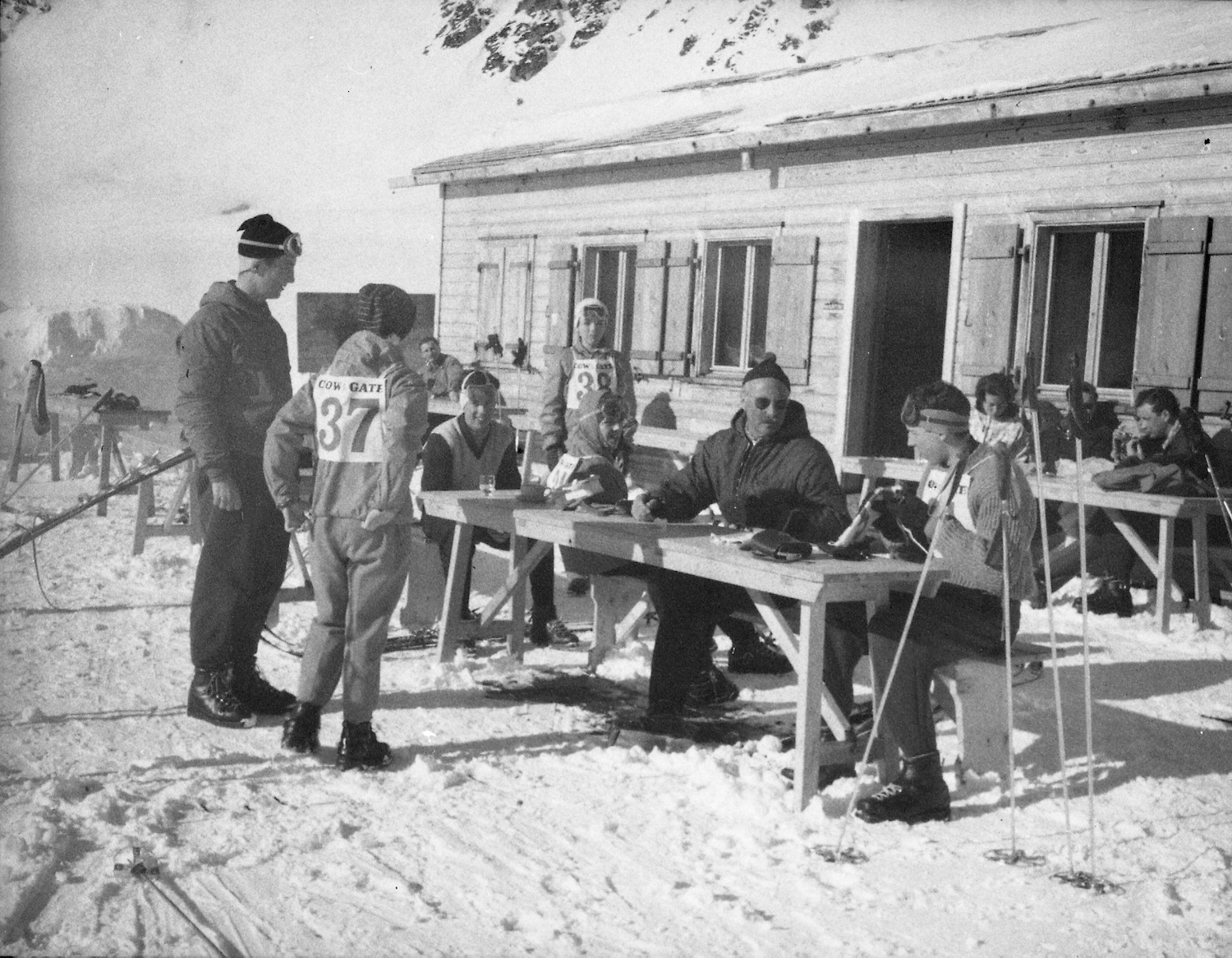 Black and white photo of skiers in Swiss Alps sitting at tables outside in the snow