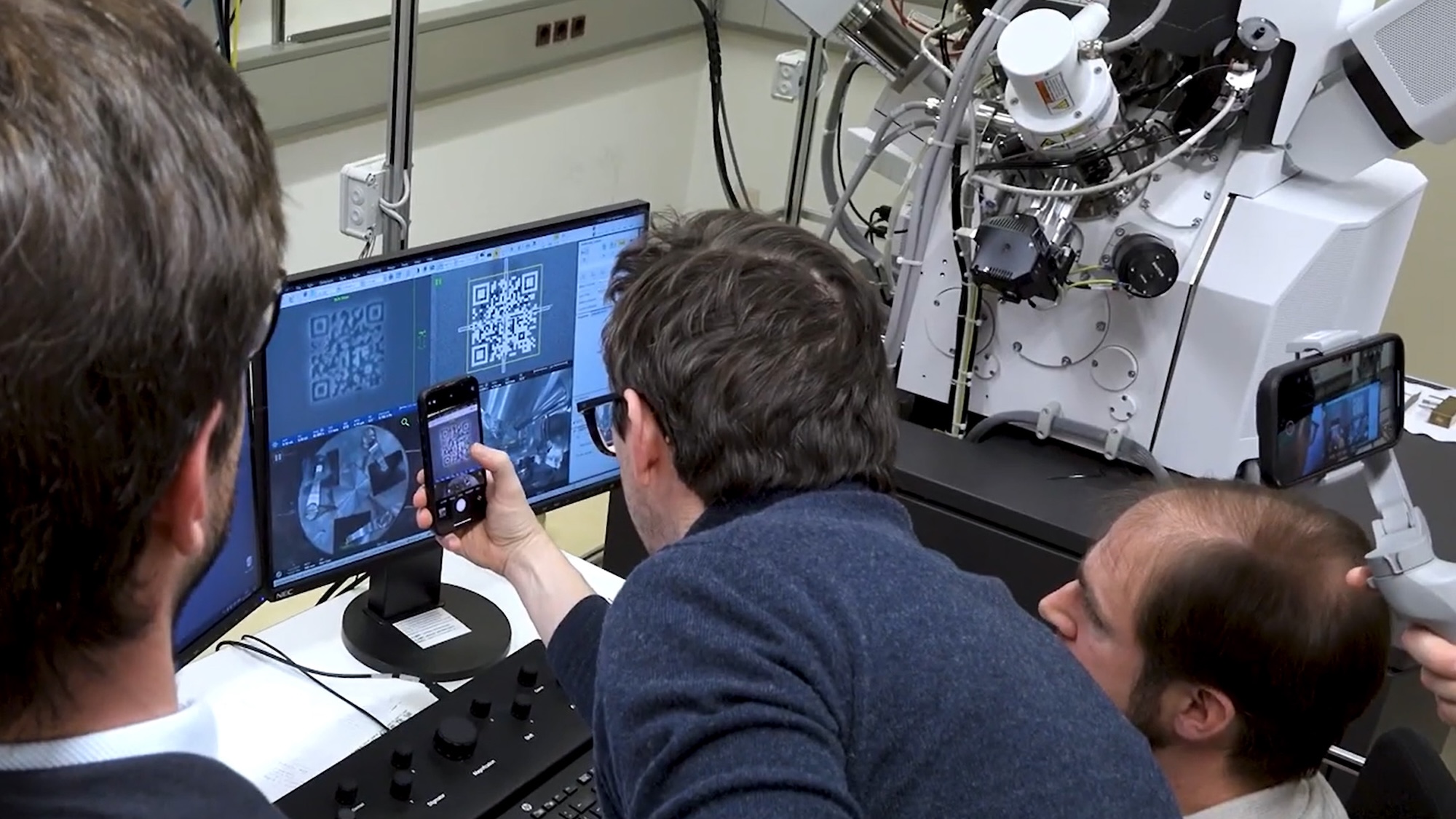 Researchers holding smartphone up to computer monitor to test world's smallest QR code