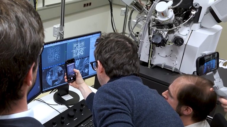 Researchers holding smartphone up to computer monitor to test world's smallest QR code