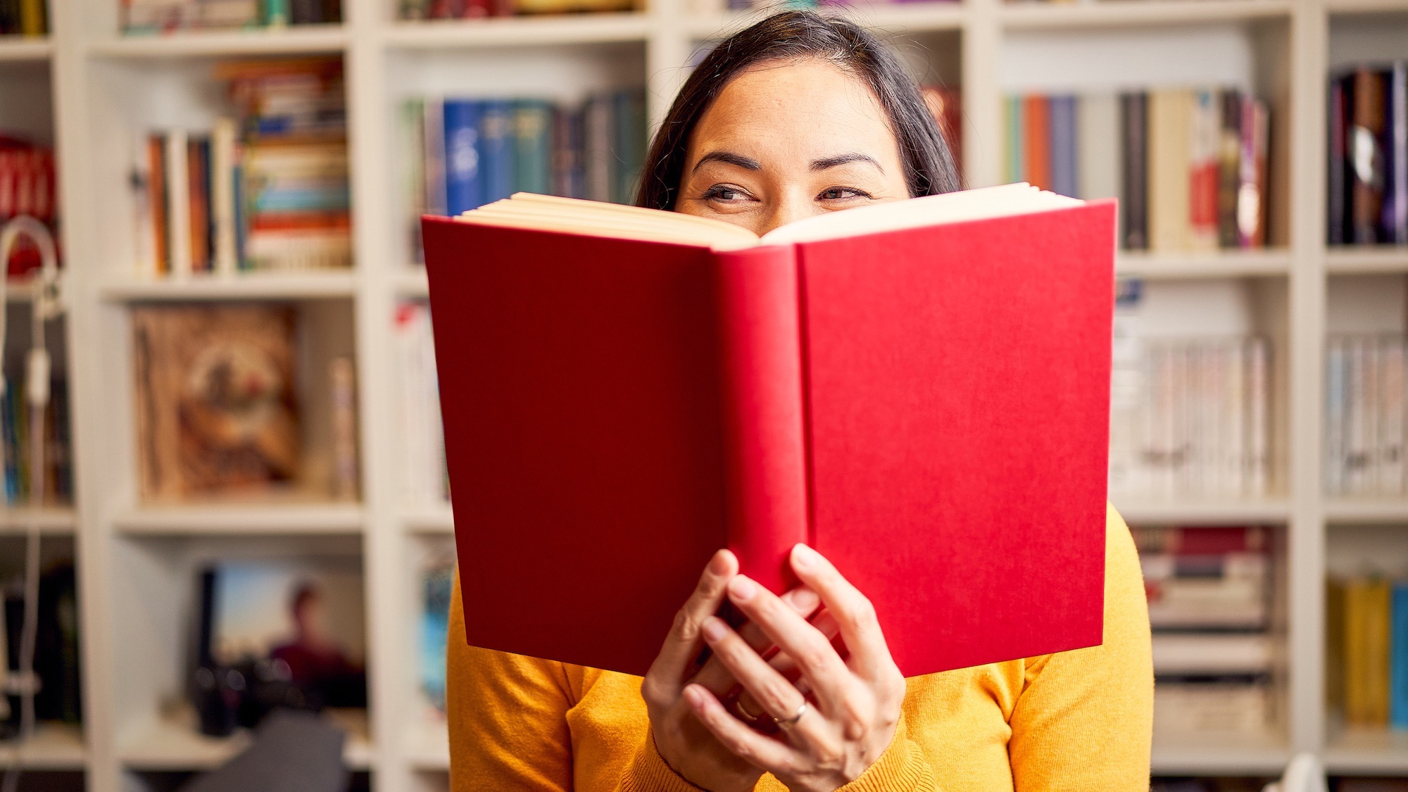 Female young behind book with face covered for a red book while smiling