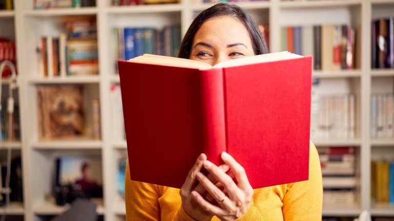 Female young behind book with face covered for a red book while smiling