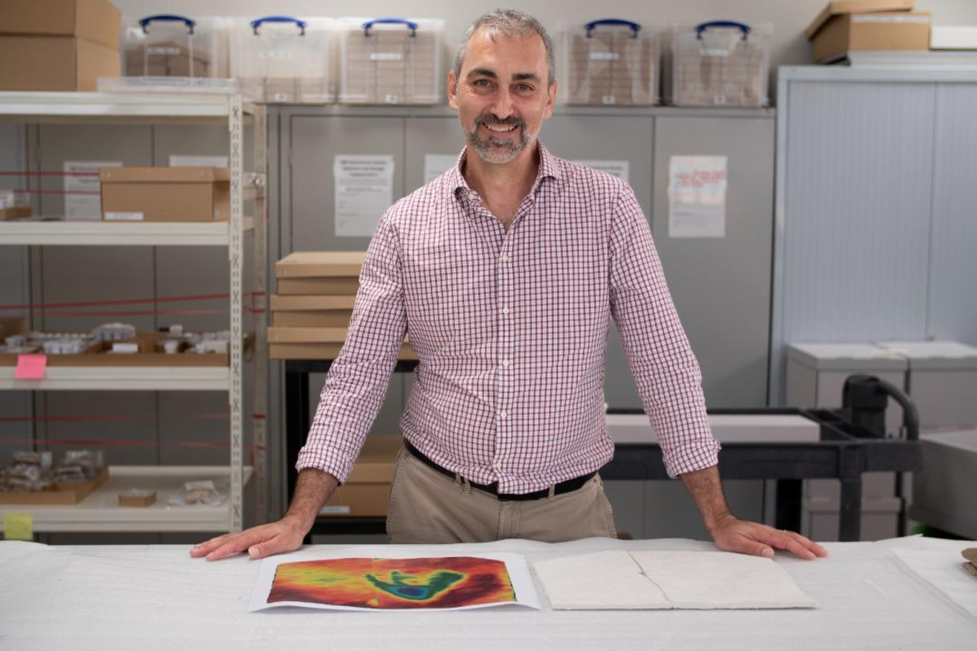 a man stands on a lab table with a print out of a fossil