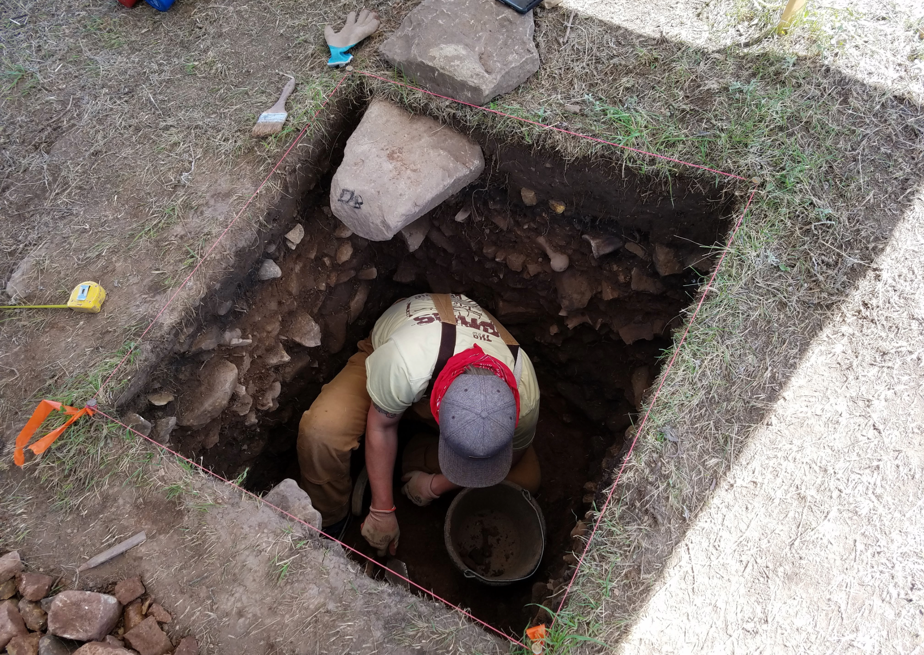 a student digging for archeological finds in a hole dug into the ground
