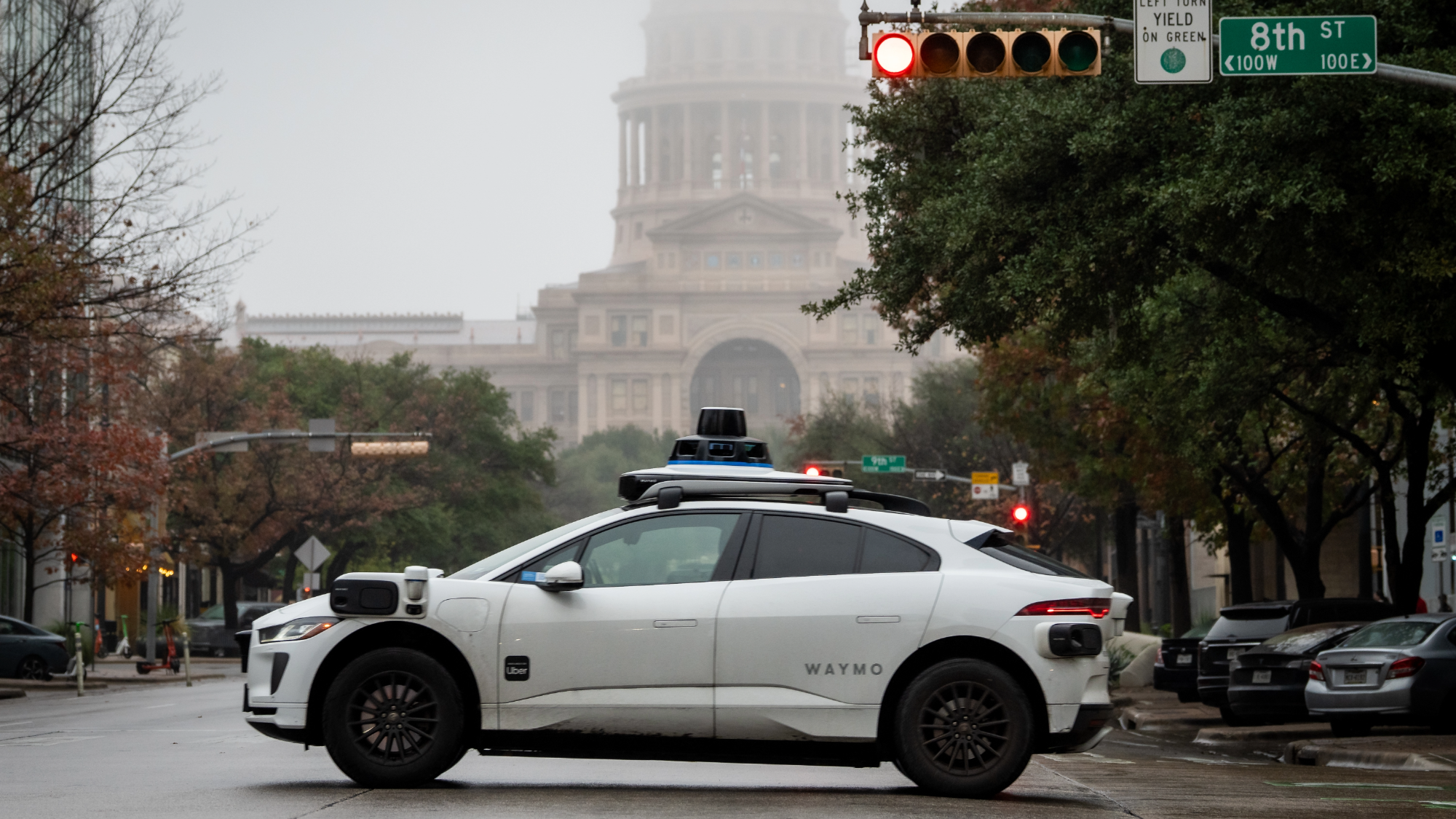 a white driverless car drives in front of a large state capitol building