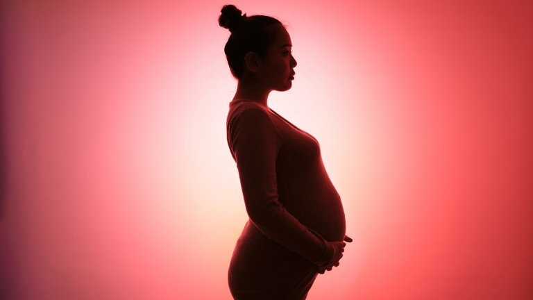 A side-profile silhouette of a pregnant woman standing against a vibrant pink and orange gradient background.