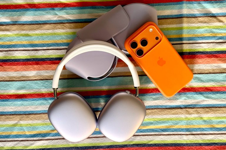 Purple AirPod Max 2 headphones shown next to a Cosmic Orange iPhone 17 Pro on a colorful tablecloth