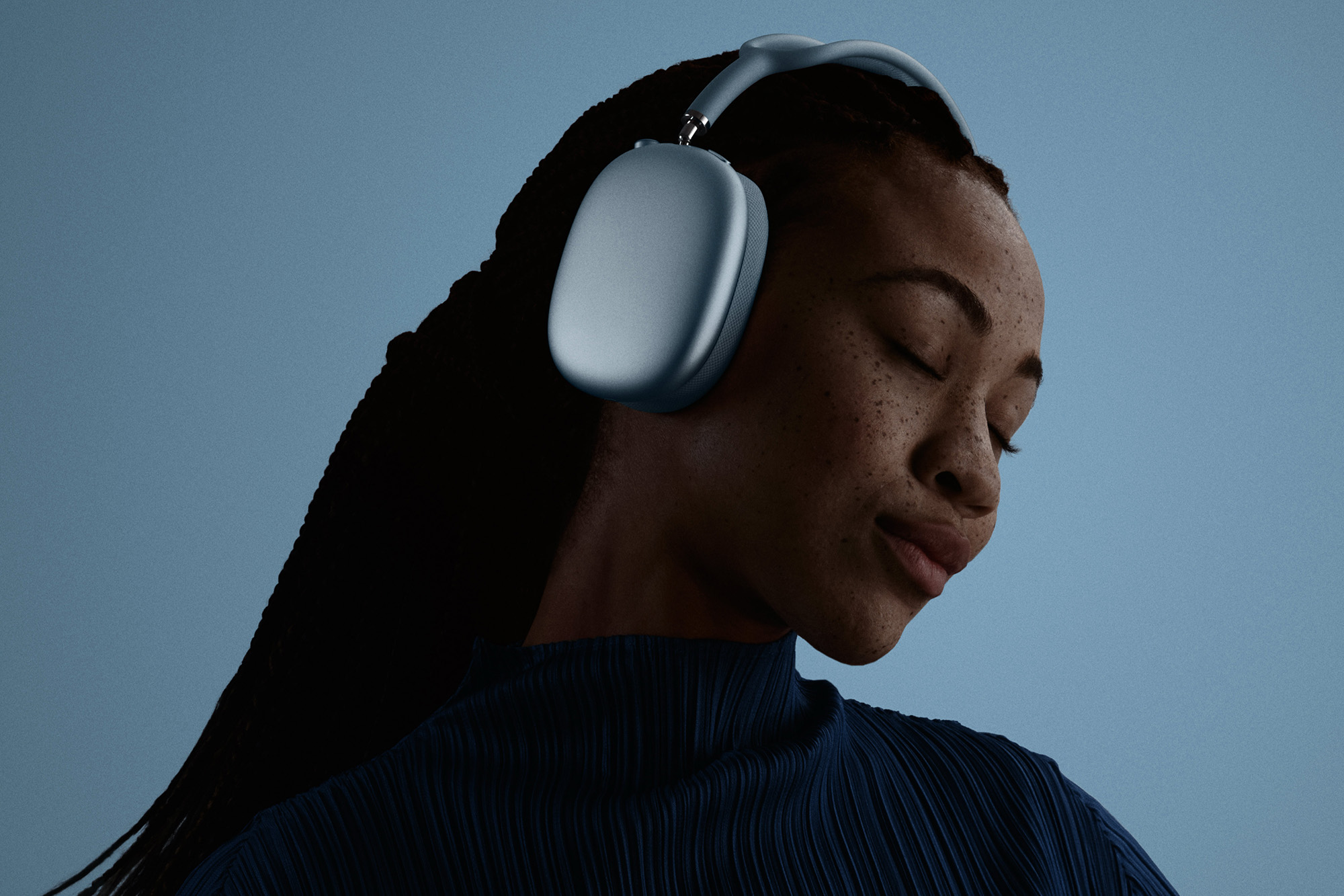 A female model showing off lite blue AirPods Max 2 headphones in a promotional image from Apple