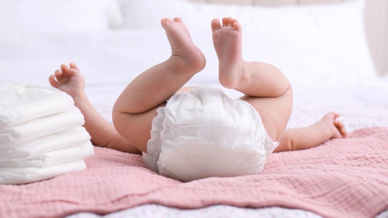 Little baby and stack of diapers on bed, closeup