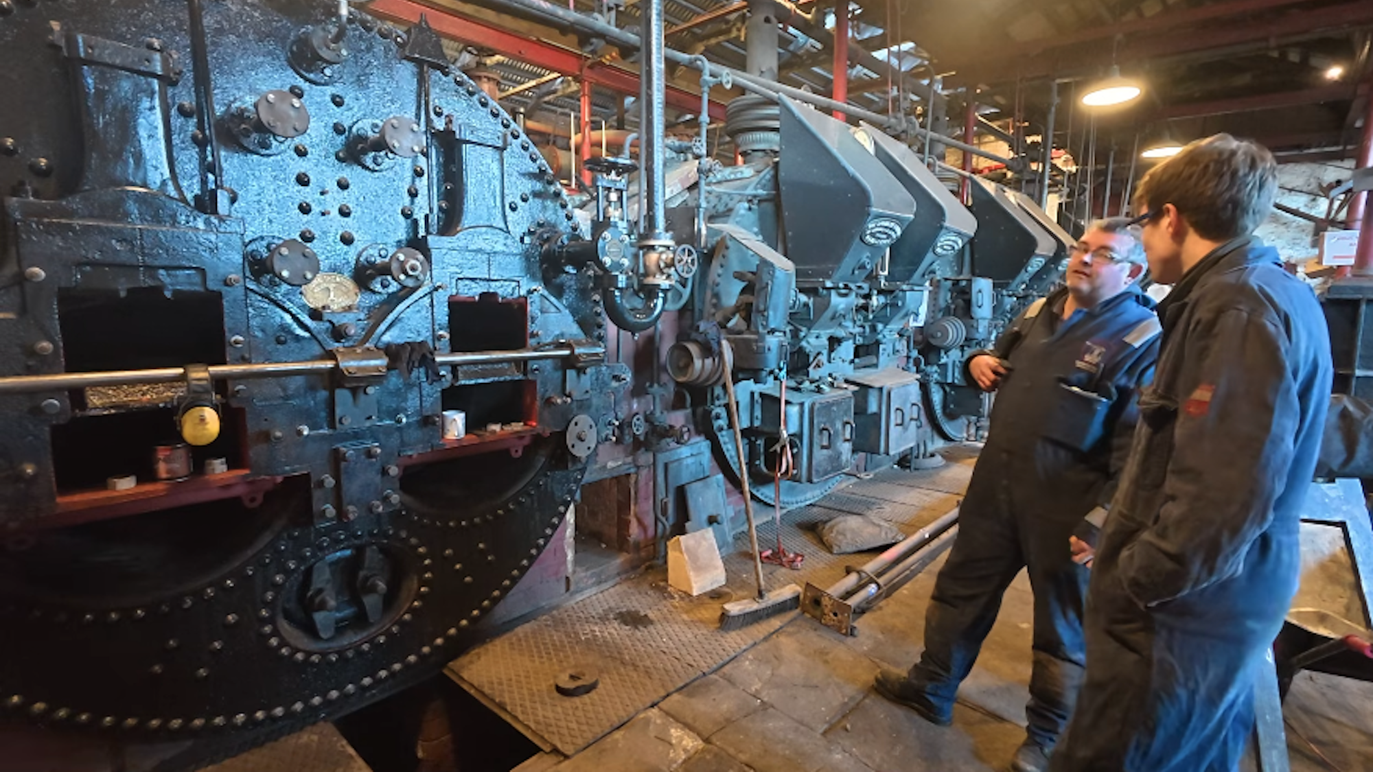 Two men standing next to boiler setup in pump station