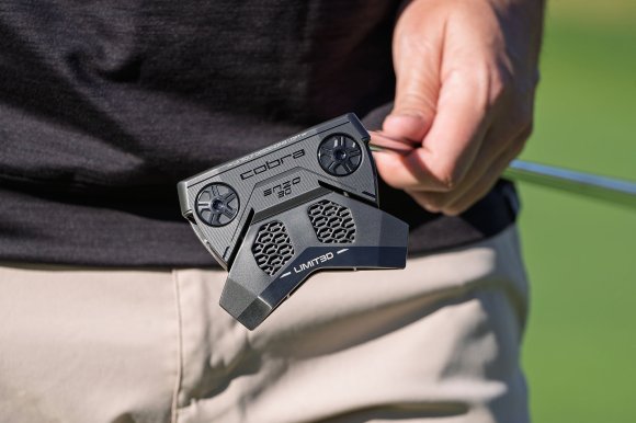 A golfer on the green holding a LIMIT3D ENZO mallet-style putter in the sun so you can see the 3D-printed lattice through the bottom.
